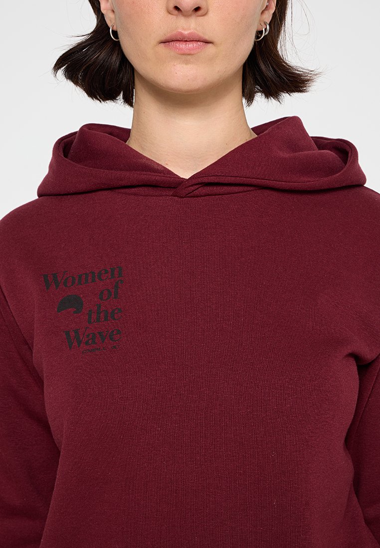 Kastanienfarbene Kapuzenjacke mit einer Vorderseite-Kängurutasche, mit einem schwarzen Grafikschriftzug "Women of the Wave". Weicher Stoff, lockerer Schnitt, gerippte Bündchen.