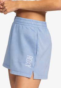 Šviesiai mėlynos sportinės šortai su elastine juostele, šoninėmis plyšio detalėmis ir baltu "ROXY" logotipo siuvinėjimu ant kairiojo šlaunies. Minkšta tekstilė.