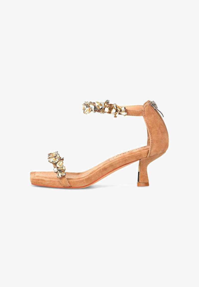 Sandales à talons hauts en suède nude avec un bout carré, une bride de cheville ornée et des gemmes décoratives. Design à petit talon bloc avec une fermeture éclair.