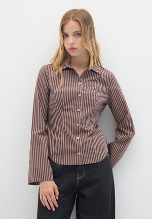 Braun-weiß gestreifte Bluse, lange Ärmel, Kragen, Knopfverschluss, taillierte Passform, glatte Textur, kombiniert mit dunklen Denim-Hosen.
