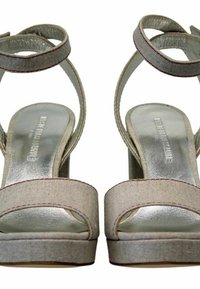 Sandales à plateforme beiges avec une lanière métallique lisse, dessus en tissu et semelle texturée. Comprend deux lanières croisées et un soutien de la cheville.