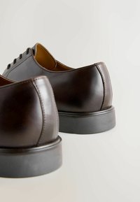 Braune Lederkleidschuhe mit glatter Oberfläche, runder Zehenform und schwarzen Gummisohlen. Detaillierte Naht entlang der Naht.