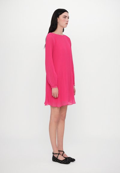 Fuchsia geplooide jurk met lange mouwen, ronde halslijn en uitlopende zoom. Gecombineerd met zwarte ballerina's met een gestikte ontwerpelement.