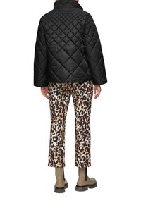 Zwarte gewatteerde jas met een hoge kraag, gecombineerd met broek van luipaardprint met beige en bruine vlekken op een crèmekleurige achtergrond. Enkelboots zichtbaar.