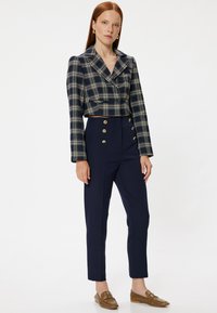 Gekürzter marineblauer kariert Blazer mit goldenen Knöpfen, kombiniert mit hochgeschnittenen marineblauen Hosen, die ähnliche Knopfakzente aufweisen, und braunen Loafers.