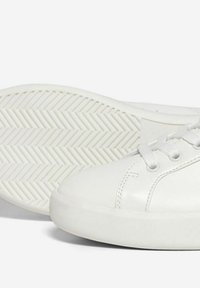 Sneaker bianco con tomaia in pelle liscia, punta tonda e suola piatta in gomma con motivo a spina di pesce. Chiusura con lacci visibile.