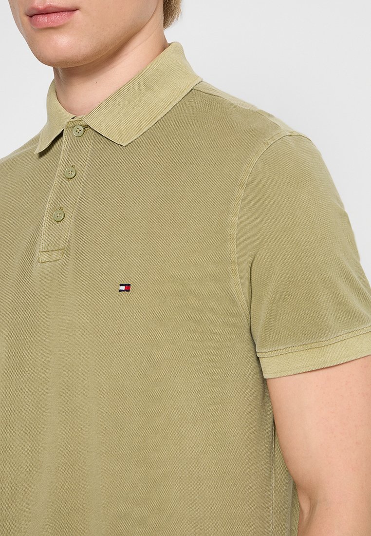 Polo de color verde oliva con un acabado texturizado, cuello puntiagudo, tapeta de tres botones y un pequeño logo bordado en el lado izquierdo del pecho.