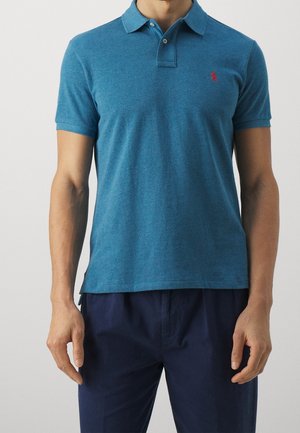 Turkusowa koszulka polo wykonana z miękkiego materiału, z trzyprzyciskową listwą, krótkimi rękawami i małym czerwonym logo na lewej piersi.