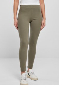 Olijfgroene leggings van rekbaar materiaal, met een hoge taille en een gladde textuur. Gekocht met witte sneakers.