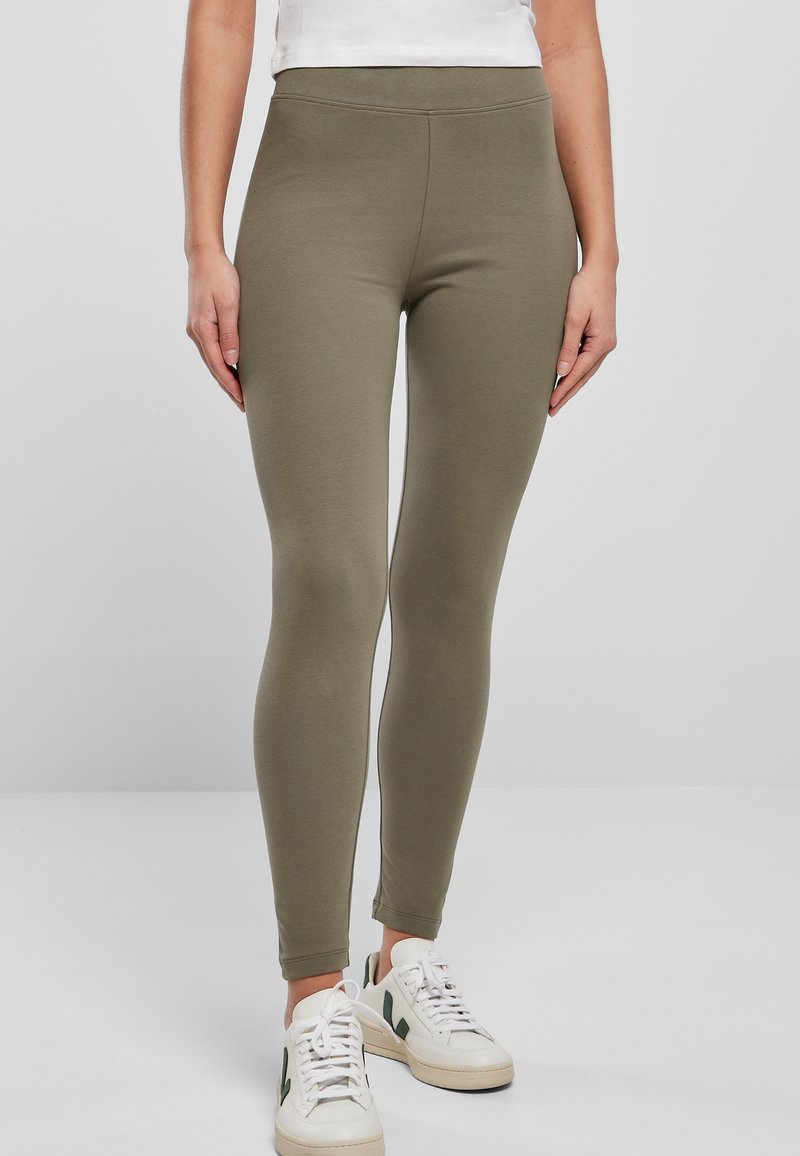Olijfgroene leggings van rekbaar materiaal, met een hoge taille en een gladde textuur. Gekocht met witte sneakers.