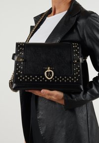 Borsa a tracolla nera strutturata con accenti di borchie dorate, tracolla a catena e chiusura decorativa. Materiale testurizzato e finitura liscia.