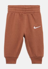 Rjave otroške trenirke z elastičnim pasom in manšetami, z belo Nike Swoosh logotipom na levi stegni.