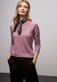 Top rosa de manga larga con cuello redondo, combinado con pantalones marrón oscuro. Un pañuelo negro con estampado de leopardo está atado alrededor del cuello.