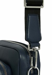 Bolso de cuero azul con acabado texturizado, que presenta herrajes plateados, un compartimento con cremallera y una correa negra ajustable con un clasp metálico.