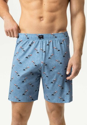 Uomo che indossa boxer blu con un piccolo motivo di uomo subacqueo che tiene boe rosse e bianche, che si sistema la cintura con la mano sinistra.
