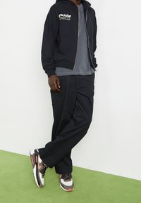 Svart zip-up hoodie med logotyp, grå t-shirt, lösa svarta byxor och sneakers med vita, bruna och rosa accenter. Släta texturer.