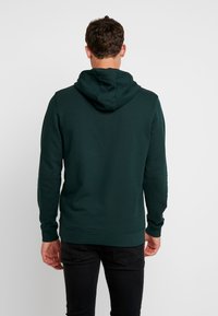 Sudadera verde oscuro con capucha ajustable, puños y dobladillo acanalados. Textura suave, diseño ajustado y estilo minimalista.
