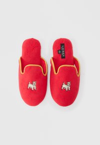 Par de chinelos de veludo vermelhos com acabamento amarelo, cada um apresentando um cão pequeno branco bordado na frente e uma etiqueta de marca visível no interior.