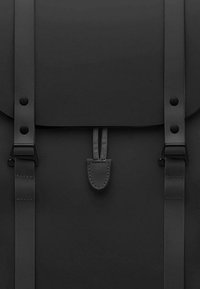 Zaino nero con finitura opaca liscia, dotato di spallacci regolabili, chiusura a patta e dettagli in pelle. Design minimalista.