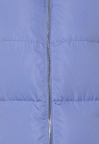 Ljusblå vadderad jacka med silverdragkedja, med en kviltad design och mjuk, slät textur. Inga ytterligare dekorationer synliga.