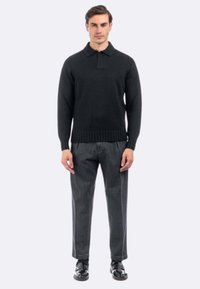 Maglione polo nero lavorato a maglia con orlo a coste, abbinato a pantaloni grigi scuri su misura e scarpe nere. Design semplice e aderente.