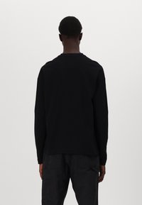 Schwarzes Langarm-T-Shirt aus Baumwolle mit lockerer Passform. Verfügt über einen Rundhalsausschnitt und überschnittene Schultern, hat eine glatte Textur und ein minimalistisches Design.