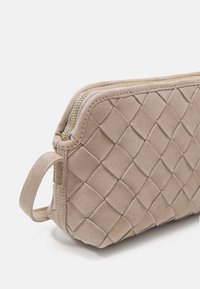 Busta in suede beige con motivo trapuntato, chiusura con zip dorata e manico laterale. Texture liscia, forma rettangolare e dettagli di cucitura sottili.