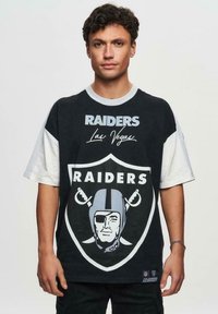 Svart och vit oversized t-shirt med texten "Raiders" och "Las Vegas", med en stor logotyp som visar en fotbollshjälm och ansikte.