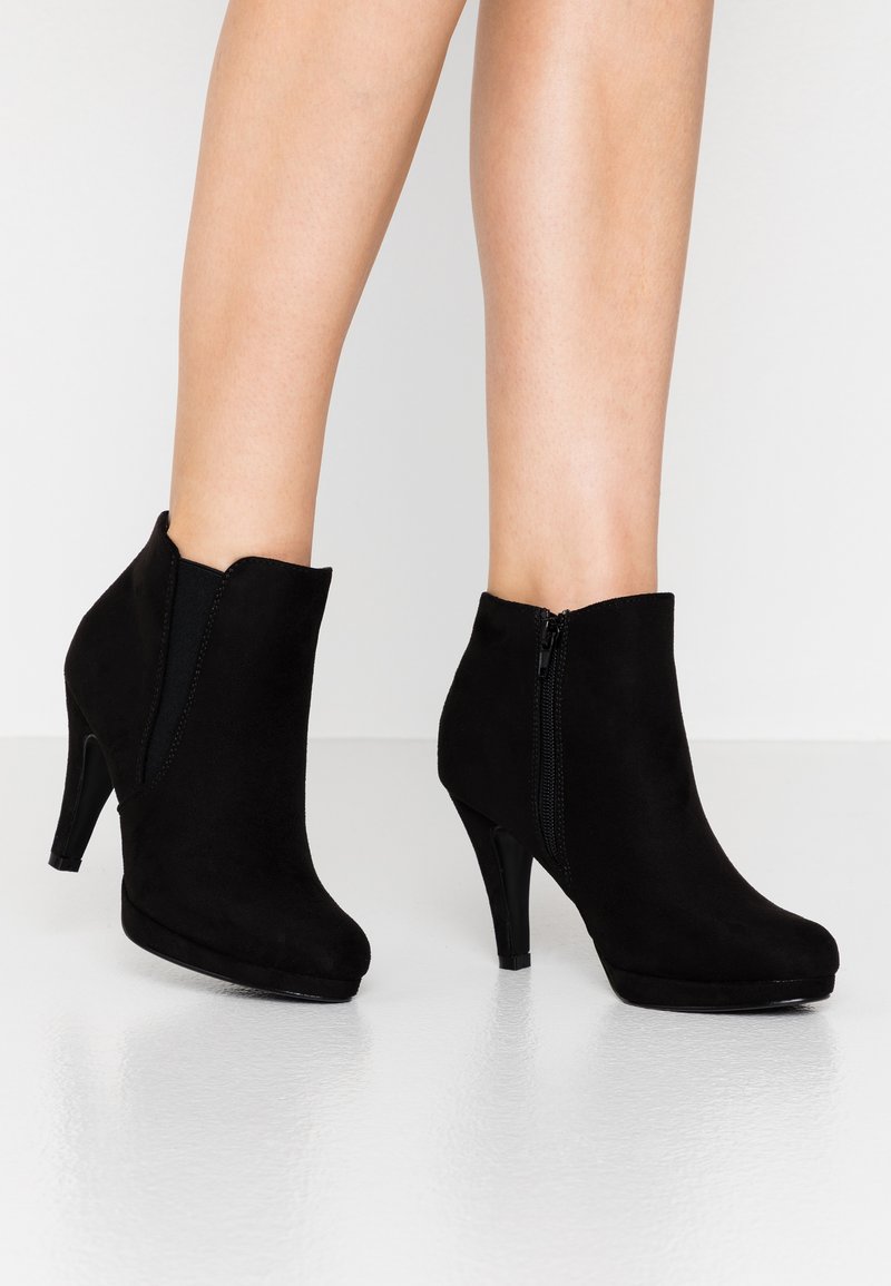 Bottines en nubuck noir avec un design ajusté, un talon haut, une fermeture éclair sur le côté et une texture lisse. Bout arrondi et silhouette élancée.