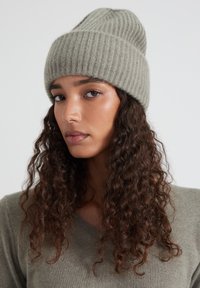 Beanie in maglia a coste grigio chiaro con una vestibilità aderente. Il tessuto presenta una trama morbida e il design si inclina dolcemente nella parte superiore.