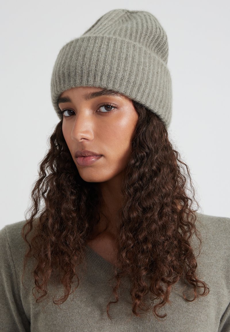 Beanie in maglia a coste grigio chiaro con una vestibilità aderente. Il tessuto presenta una trama morbida e il design si inclina dolcemente nella parte superiore.