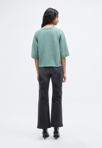 Sweat-shirt vert raccourci avec manches tombantes, tissu texturé ; associé à un jean noir taille haute et des bottes à talons noires.