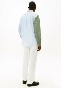 Jasnoniebieska i zielona koszula w paski z kołnierzykiem zapinanym na guziki oraz rękawami w kontrastującym kolorze, zestawiona z białymi spodniami i czarnymi butami.