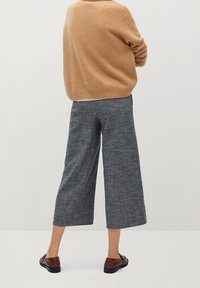 Beżowy sweter dzianinowy w połączeniu z szerokimi, teksturowanymi spodniami w czarno-białą kratę oraz brązowymi butami wsuwanymi.