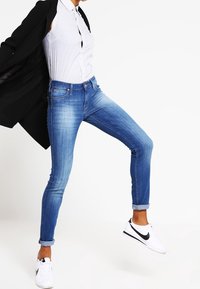 Smala blå jeans med en bleknad tvätt, fem fickor, bältesöglor, uppvikt fåll, som bärs med en randig skjorta och vita sneakers.