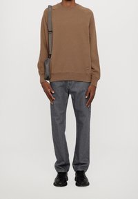 Bruine sweatshirt met een ronde hals, raglanmouwen, gecombineerd met grijze spijkerbroek. Afgewerkt met zwarte schoenen en een grijze schoudertas.