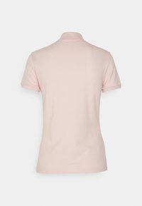 Polo manches courtes rose clair vu de dos avec un col classique sur un fond uni.