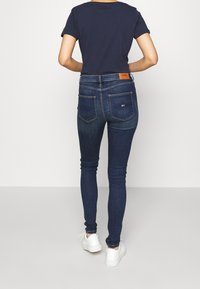 Jeans ajustados de mezclilla azul oscuro con un desvanecido sutil, con cintura alta y bolsillos traseros, combinados con una camiseta de manga corta en azul marino.