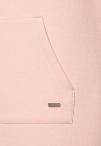 Rosa Kapuzenpullover mit einer Kängurutasche und einem silbernen Logo-Label. Der Stoff hat eine glatte Textur und saubere Nähte.