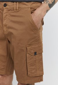 Brune cargo shorts laget av bomull, med sidelommer, en avslappet passform og sømdetaljer. Stoffet har en jevn tekstur.