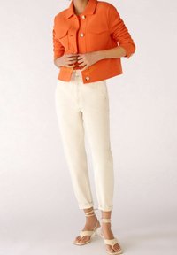 Orange texturerad jacka med guldknappar, ihopparad med krämfärgade smalna byxor. Off-white snörskor fulländar outfiten.