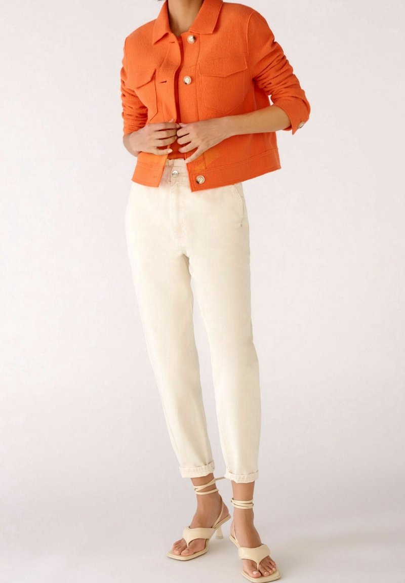 Orange texturerad jacka med guldknappar, ihopparad med krämfärgade smalna byxor. Off-white snörskor fulländar outfiten.