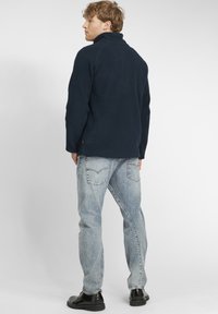 Navy fleece pullover with a high collar, textured fabric, and relaxed fit. Paired with light blue jeans and black shoes.