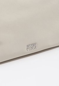 Jasnoszara torebka o fakturowanej powierzchni, wykonana z miękkiego materiału tekstylnego. Na przedniej części znajduje się srebrne logo "BIMBA Y LOLA".