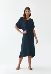 Tummansininen polvipituinen mekko, jossa on rento malli, lyhyet hihat ja hienovarainen epäsymmetrinen helma. Valmistettu sileästä, kevyestä kankaasta.