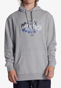 Persoon draagt een grijze hoodie met een voorzak, met grote tekst "OCTAHOES" en een skateboardafbeelding in de letters.