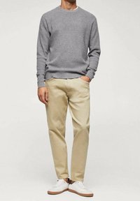 Suéter de punto gris, pantalones beige y zapatillas blancas. Textura suave con cuello redondo. Corte casual sin patrones visibles ni adornos.