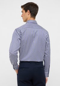 Blauw-wit gestreept overhemd met een kraag, met lange mouwen en knoopsluiting bij de manchetten, gedragen met donkere broeken.