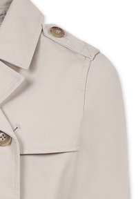 Cappotto beige con design doppiopetto, caratterizzato da grandi bottoni, colletto a punte e texture di tessuto liscia.