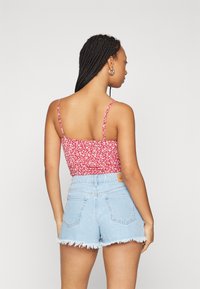Červený kvetovaný crop top s tenkými ramienkami, v kombinácii so svetlomodrými džínsovými šortkami s roztrhnutými okrajmi. Zameranie na pohľad zozadu a textúru látky.